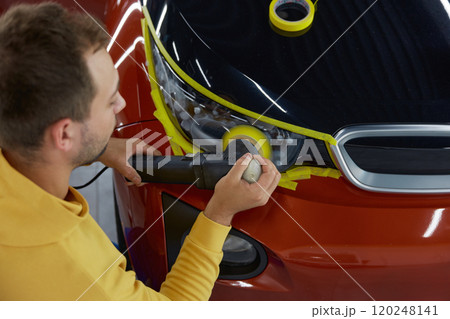 Man technician polishing headlamps at car garage workshop 120248141