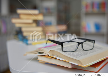 Closeup view on opened paper book with eyeglasses on library table Closeup view on opened paper book with eyeglasses on library table 120248292