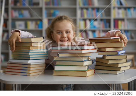 Happy glad little school girl child hugging stack of textbooks in library 120248296
