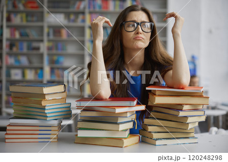 Tired woman sitting front of huge stack of book in library Tired woman sitting front of huge stack of book in library 120248298