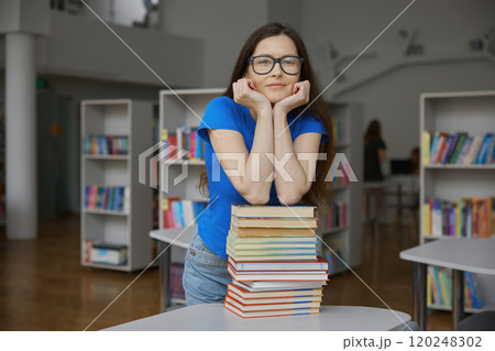 Young woman overloaded with huge stack of paper book standing over bookstore 120248302