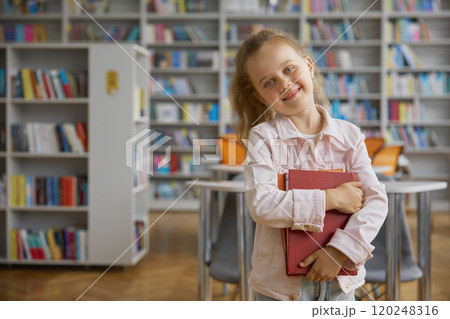Portrait of cute smart girl child over public library bookshelves background Portrait of cute smart girl child over public library bookshelves background 120248316