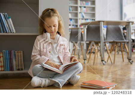 Cute curious little girl child reading book on floor of modern city bookstore 120248318