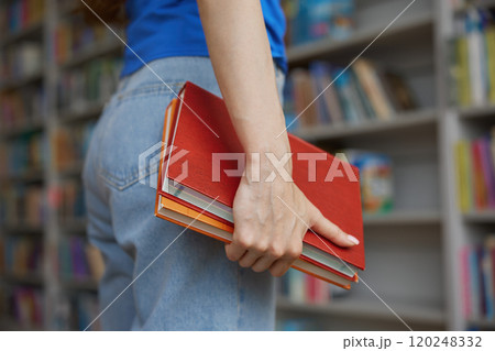 Closeup view female hands holding pair of books over bookshelves on background Closeup view female hands holding pair of books over bookshelves on background 120248332