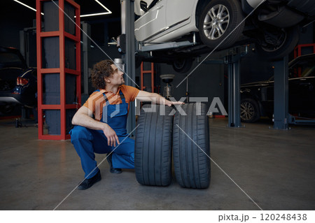 Repairman rolling car spare tires while working on wheel replacement 120248438
