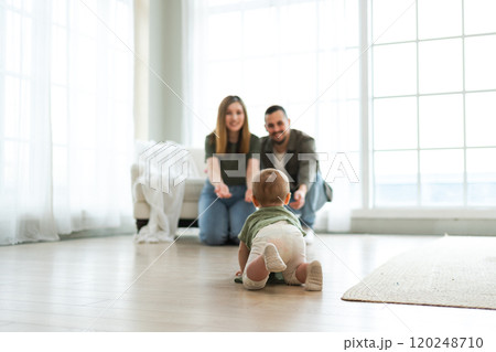 Happy family. Mother father looking at cute little toddler girl crawling on floor in bedroom. Infant baby resting playing with parents indoor at home. Mom dad newborn baby. Cute crawling child 120248710