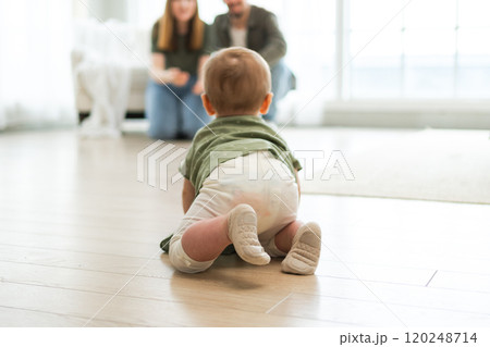 Happy family. Mother father looking at cute little toddler girl crawling on floor in bedroom. Infant baby resting playing with parents indoor at home. Mom dad newborn baby. Cute crawling child Happy family. Mother father looking at cute little toddler girl crawling on floor in bedroom. Infant baby resting playing with parents indoor at home. Mom dad newborn baby. Cute crawling child 120248714