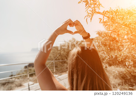 Woman Making a Heart Shape with Her Hands While Standing on a Cliff Woman Making a Heart Shape with Her Hands While Standing on a Cliff 120249136