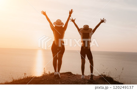 Two Women in Hats Stand Back to Back, Arms Raised in the Air Two Women in Hats Stand Back to Back, Arms Raised in the Air 120249137