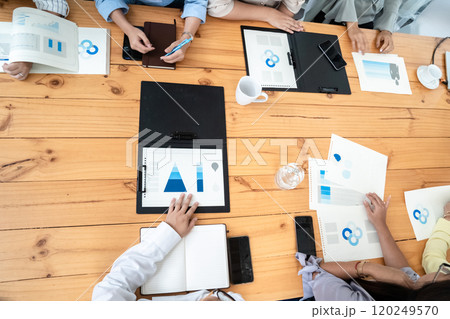 Employees Meeting in conference room. There are triangular diagrams, graphs, and related data set aside on a long brown wooden table. 120249570