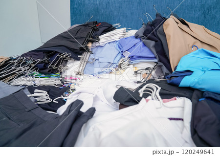 Untidy piles of clothes, arrange on a blue King bed. Women suits come in a variety of colors, but men pants were a dark tone color, all of this ready to rearrange in new closet. 120249641