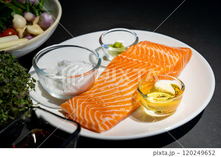 Salmon steak, Raw fillet of sea fish salmon or trout on white dish with salt, oil, and wasabi cream in studio light on dark background. Salmon steak, Raw fillet of sea fish salmon or trout on white dish with salt, oil, and wasabi cream in studio light on dark background. 120249652