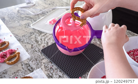 With focused attention, this budding culinary artist dips pretzels into a pot of melted chocolate, creating sweet delights in the warmth of a well-lit home kitchen. 120249757