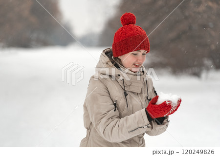 Portrait of a beautiful girl in a hat and coat and in red knitted mittens in the snow park. Portrait of a beautiful girl in a hat and coat and in red knitted mittens in the snow park. 120249826