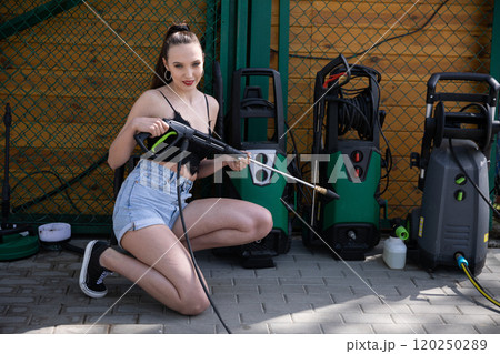 A Young Woman Enthusiastically Using a Pressure Washer in a Bright Outdoor Setting 120250289