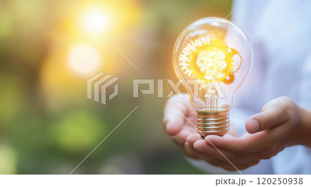 A hand cradles a light bulb of gears, symbolizing creativity and innovation against a warm glow. 120250938