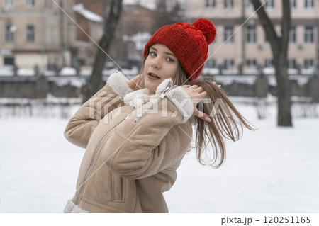 Portrait of a beautiful young girl in a beige coat and red hat on a background of winter park. Portrait of a beautiful young girl in a beige coat and red hat on a background of winter park. 120251165