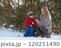 Happy mom and son with hot drinks spending time together in snowy forest. Picnic in winter outside. 120251490