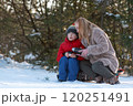 Mother and child spending time outdoors in winter. Woman pours hot tea from thermos into mug. 120251491