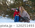 Mom and son in winter outside, mom points her hand into the distance. Picnic in snow-covered forest. Winter holidays. 120251493