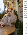 Attractive blue eyed woman stands at a table in a street cafe. Christmas holidays. Winter walk around the city. Vertical frame 120251506