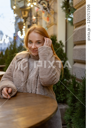 Attractive blue eyed woman stands at a table in a street cafe. Christmas holidays. Winter walk around the city. Vertical frame 120251506