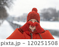 Portrait of girl in red winter jacket and woolen hat with mittens showing heart with hands. Woman in fashionable winter look outdoors 120251508
