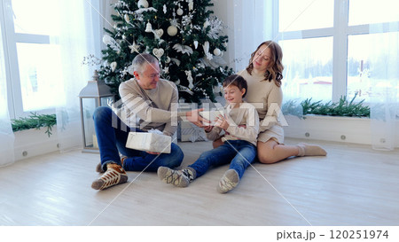 Happy family gathers around a christmas tree, sharing gifts in a cozy living room filled with festive decorations and warm light. A day with family before Christmas. New Year's Eve with family 120251974