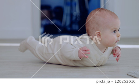 Innocent and playful, baby in a beige bodysuit lifting their head and gazing curiously. Baby crawling on the floor in a bright room 120252010