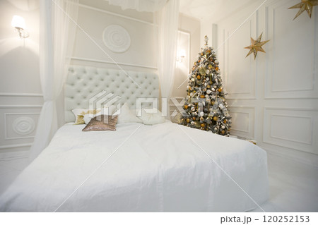 The interior of the New Year's bedroom. Room with a big white bed and a Christmas tree The interior of the New Year's bedroom. Room with a big white bed and a Christmas tree 120252153