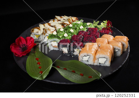Seth sushi on a black background.Menu of the Japanese restaurant. Several sushi lined on a plate decorated with a decor of red berries, a flower and leaves 120252331