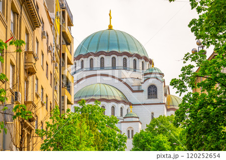 Saint Sava Cathedral stands majestically against a summer sky, surrounded by lush greenery and historical buildings. Visitors enjoy the vibrant atmosphere in Belgrade. 120252654