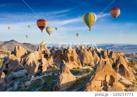 Colorful hot air balloons fly in blue sky over amazing rocky valley in Cappadocia, Turkey. 120253771