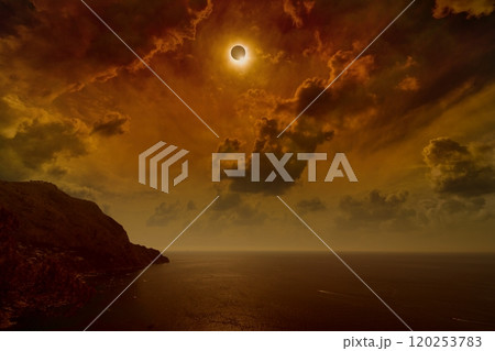 Total solar eclipse in dark red sky above sea and mountains 120253783