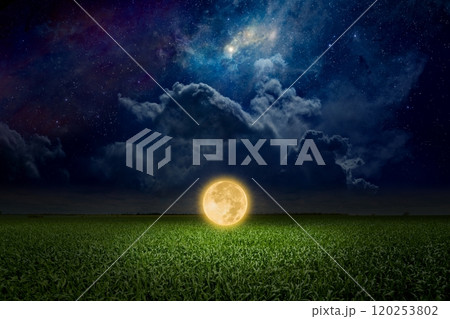 Unreal fantastic image - luminous sphere, similar to full moon, levitates over green field. Bright stars, glowing nebula and clouds in dark blue sky. 120253802