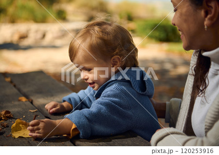 Joyful toddler playing with fallen leaves on picnic table Joyful toddler playing with fallen leaves on picnic table 120253916