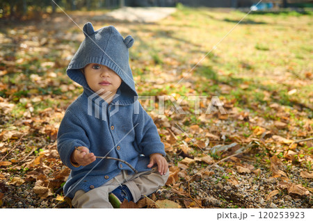 Adorable child in blue hooded sweater sitting outdoors on autumn day 120253923