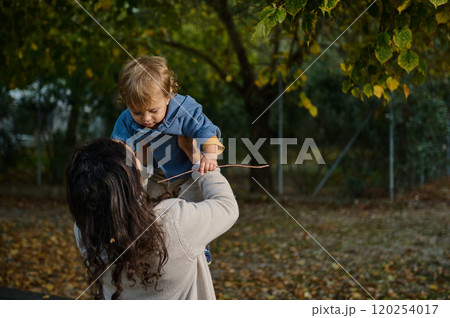 Mother lifting her playful child in a park during autumn Mother lifting her playful child in a park during autumn 120254017