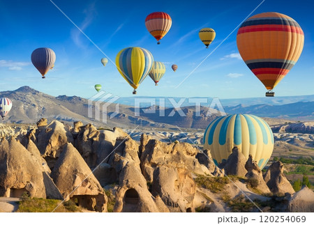 Colorful hot air balloons fly in blue sky over amazing rocky valley in Cappadocia, Turkey. 120254069