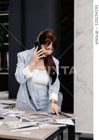 Businesswoman talking on phone while reviewing documents in modern office 120254191