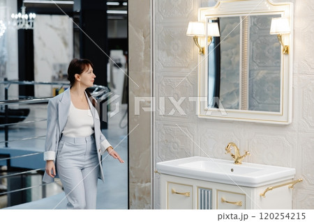 Woman in light suit stands near a freestanding bathtub in a modern showroom 120254215