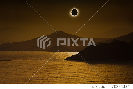 Total solar eclipse in dark red sky above mountains and sea 120254384
