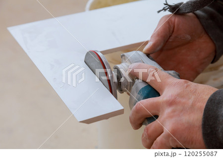Craftsperson focuses on sanding ceramic tile with power tool in workshop. 120255087