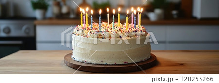 A decorated birthday cake with lit candles on a wooden board in a cozy kitchen setting A decorated birthday cake with lit candles on a wooden board in a cozy kitchen setting 120255266