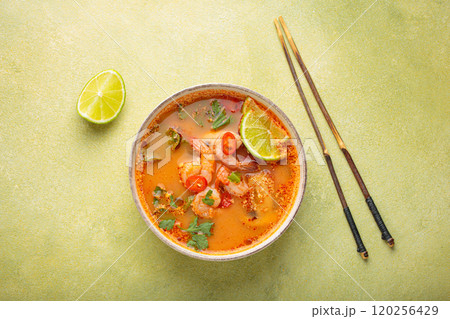 Tom yum soup with shrimps, lime, chili pepper and cilantro is served in bowl with chopsticks, traditional Thai cuisine 120256429