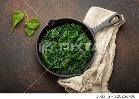 Healthy steamed spinach in cast iron pan on brown rustic background top view 120256430