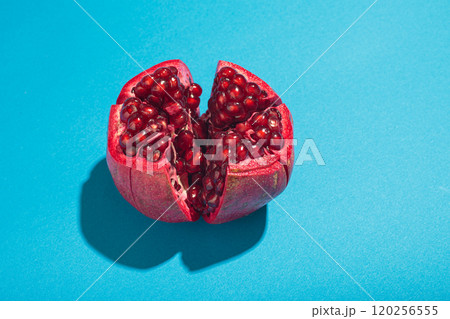 Ripe pomegranate cut opened on vibrant blue background, high contrast with hard light Ripe pomegranate cut opened on vibrant blue background, high contrast with hard light 120256555