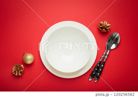 Christmas table setting with empty white plate, fir branch and golden pine cones on red background 120256562