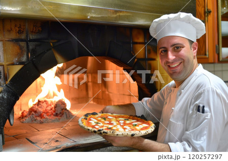 The chef Man smiling at a table with pizza, plant, and cheese in front of him 120257297