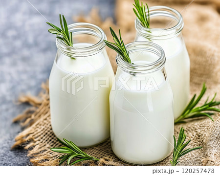 Three bottles of milk with sprigs of rosemary on a rustic burlap cloth 120257478